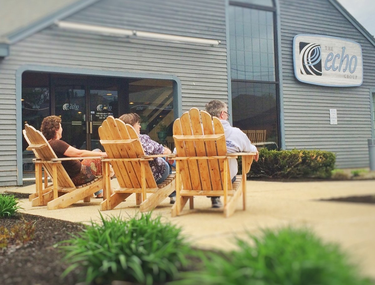 People sitting in wooden chairs outside of The Echo Group